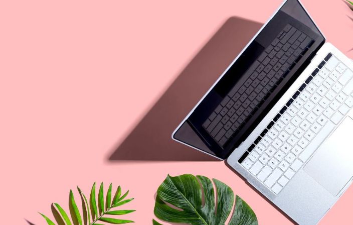 Ein offener Laptop steht auf einem pinken Tisch. Der Blickwinkel ist von oben.